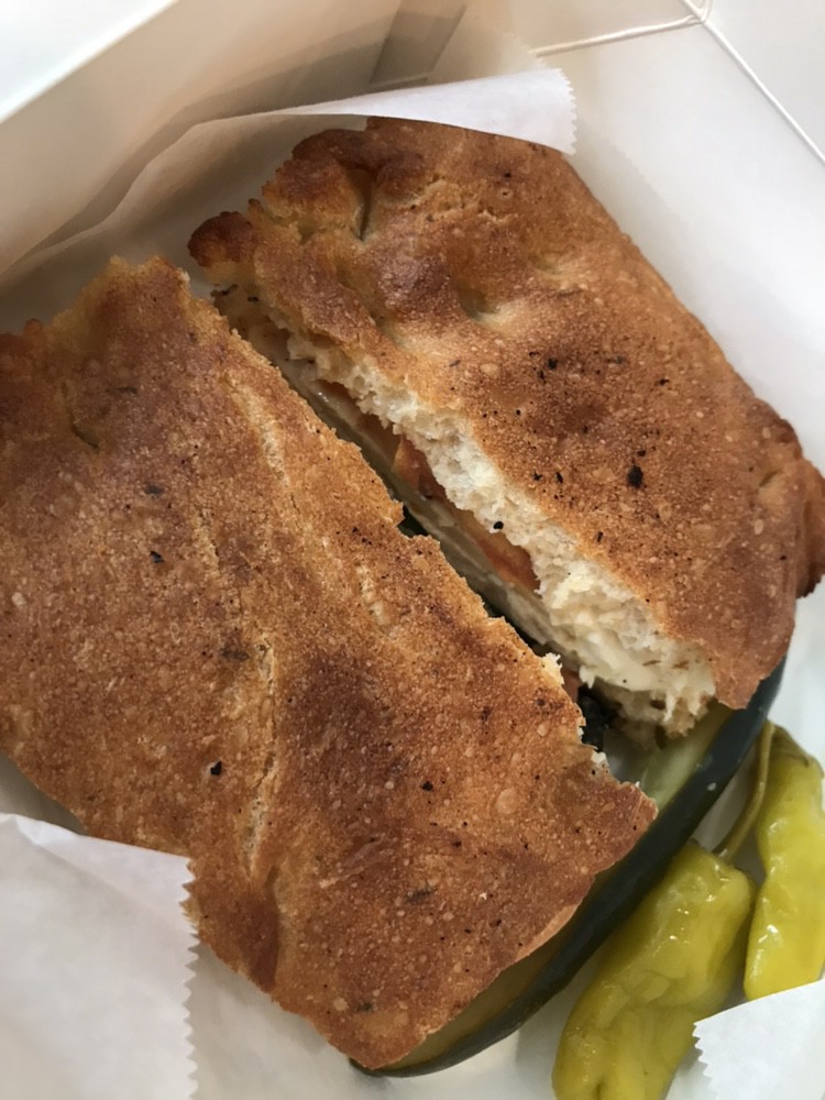 A chicken pesto sandwich with pickled peppers on the side